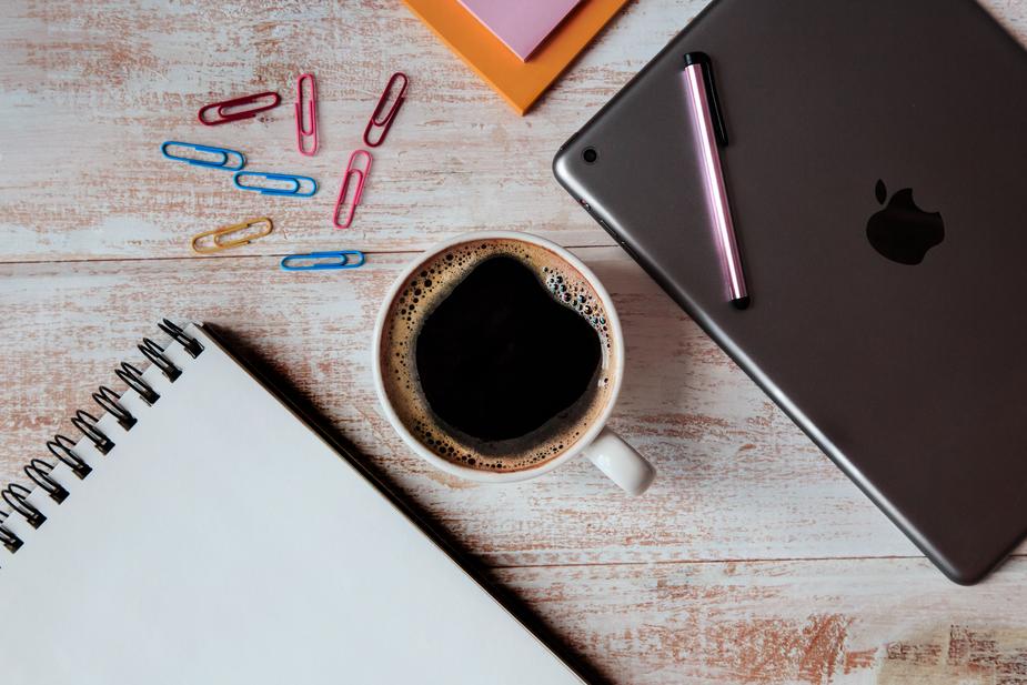 Workspace essentials like a tablet, notebook, pen, paper clips, and a cup of coffee.